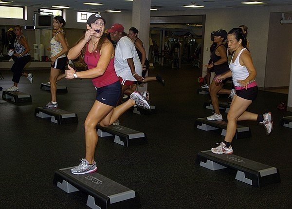 A step aerobics exercise instructor in the United States Army motivates her class to keep up the pace.