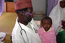 Child sits with a doctor to receive medical care A young girl sits with a doctor receiving medical care.jpg