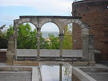 Archi a ferro di cavallo in pietra;  a destra, una torre del recinto medievale, da cui partiva anche la cinta muraria dei canonici e in primo piano una vasca di recente costruzione.