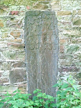 Fotografía de una piedra vertical insertada en una pared y grabada en la parte superior