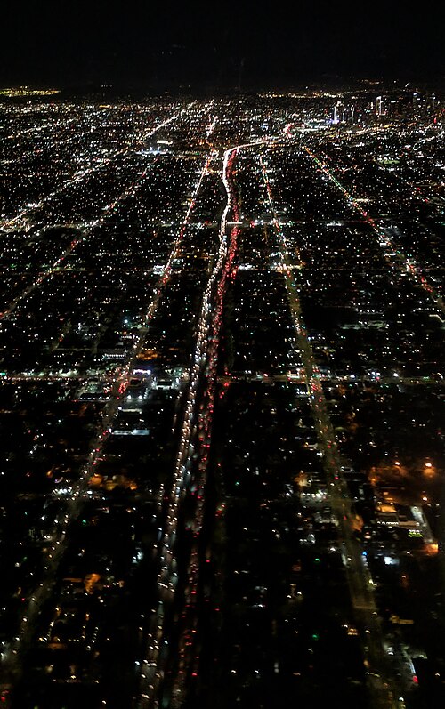 Figueroa Street (left), Harbor Freeway (center), and S Broadway (right) night aerial from the south, with downtown Los Angeles in the distance. Figuer