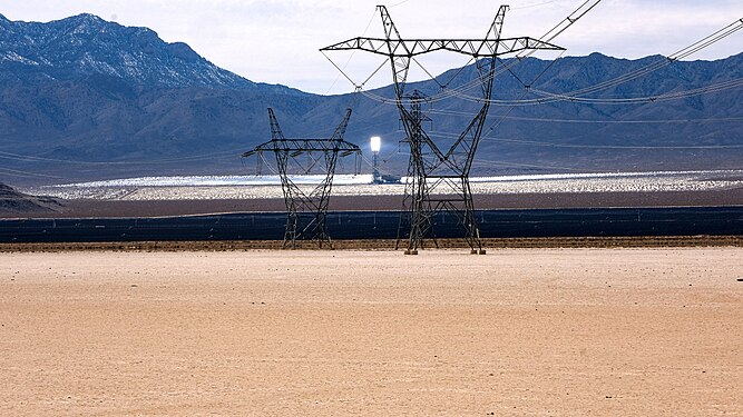 One of three solar collection towers of the Ivanpah power plant (California) glowing white in the background between transmission lines