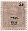 A faded looking postage stamp showing a mustachioed man with the words Nyassa and Moçambique overprinted low in the centre and 2½ in the top right