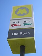 A station sign with a large yellow 'M' logo and the name 'Old Roan' underneath. Icons mark rail and bus services.