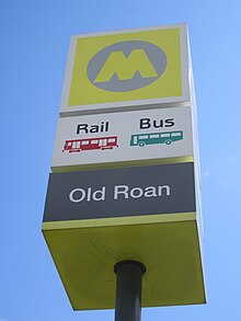 Büyük sarı bir 'M' logosu ve altında 'Old Roan' adı bulunan bir istasyon işareti.  Simgeler demiryolu ve otobüs hizmetlerini işaretler.