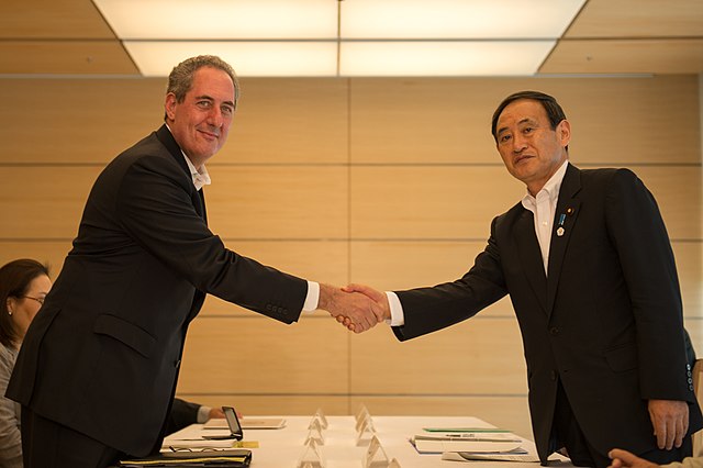 Suga (right) shaking hands with U.S. Trade Representative Michael Froman in 2013