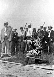 Foto eines knienden Mannes, der einen Bogen schießt und traditionelle Kleidung trägt
