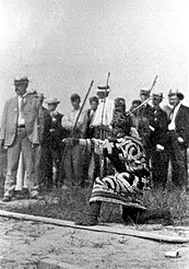 Foto van een knielende man die een boog schiet en traditionele kleding draagt