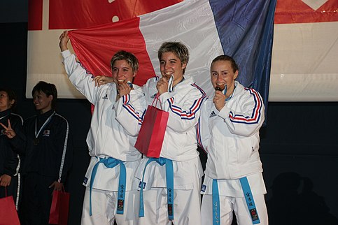 L'équipe de France de kata féminin victorieuse aux championnats du monde de karaté seniors 2006. À gauche : Jessica Buil. Au milieu : Sabrina Buil. Les trois gagnantes, joyeuses, mordent joyeusement dans leurs médailles d'or.