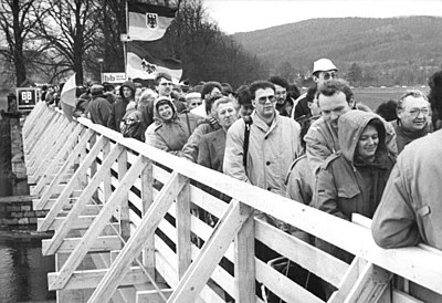 A new border crossing for pedestrians across the Inner German border linking Lauchröden in Gerstungen municipality, and Herleshausen. This temporary bridge was built immediately after the reopening of the border at the site of an old bridge across the Werra which was destroyed in the Second World War. Here, visitors are queueing to enter East Germany on 23 December 1989.