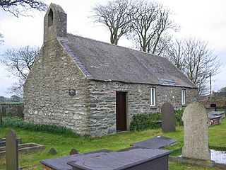 A small plain stone church seen from an angle with a bellcote on the near gable, and a simple door and two windows along the side