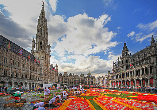 Großer Platz in Brüssel mit Rathaus (links) und Haus der Könige (rechts). Auf dem Platz legen Helfer*innen den Blumenteppich an. Grand Place Bruselas