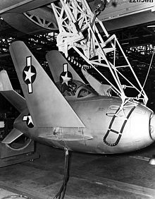 Photographie en noir et blanc du petit chasseur en forme d'œuf accroché à un trapèze, en dessous d'un grand bombardier.