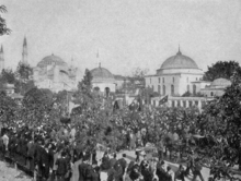 Schwarzweißfoto: eine Menschenmenge auf der Straße vor gewölbten Gebäuden und Minaretten