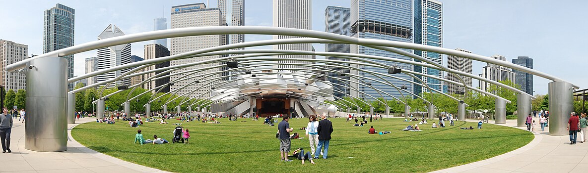 Vue futuriste d'une pelouse verte avec des gens éparpillés dessus, sous un treillis métallique soutenu par des piliers en métal brillant.  Le treillis mène à un bandshell entouré de plaques incurvées de métal brillant, avec de nombreux gratte-ciel en arrière-plan.