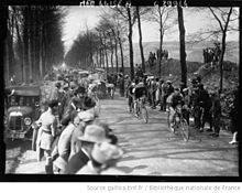 Photographie en noir et blanc montrant des coureurs cyclistes encouragés par la foule.