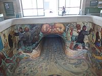 The mural features two hands holding water, which flows to other painted scenes. To the right, a man holding a pickaxe, a man giving water to a girl; to the left, a man giving water to an old woman and a man is operating a construction equipment tool. Painted on the floor, there are several aquatic species, including mollusks and plants.