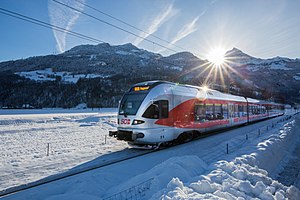 Zilveren en rode trein naast racen langs een besneeuwd veld met bergen op de achtergrond