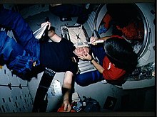 STS-41 crewmembers conduct Detailed Supplementary Objective (DSO) 472, Intraocular Pressure on the middeck of Discovery, Orbiter Vehicle (OV) 103. Mission Specialist (MS) William M. Shepherd rests his head on the stowed treadmill while Pilot Robert D. Cabana, holding Shepherd's eye open, prepares to measure Shepherd's intraocular pressure using a tonometer (in his right hand). STS-41 IOP Test.jpg