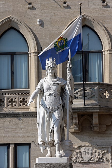 The San Marino flag behind the Statua della Libertà; this appears to be a version with a darker shade of blue than specified in law.