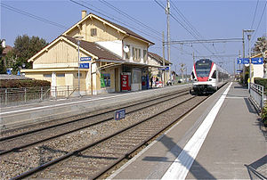 Çift hatlı demiryolu hattının yanında üçgen çatılı ve yan platformlu iki katlı bina