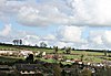 Várias casas, muitas com paredes brancas e telhados vermelhos aninhadas em um vale verde com árvores ocasionais.