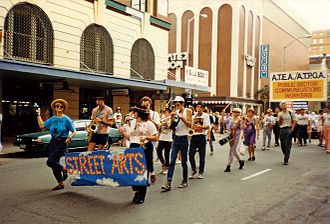 Street arts members participating in a May Day March 1988, photographer unknown, from the LHMU Queensland collection. From left Fiona Winning, Denis Peel playing saxophone, Katrina Devery, Derek Ives with cornet, Chris Sleight with saxophone, Meg Kanowski with drum, Pauline Peel, Gavan Fenelon, Alan (Fox) Rogers. The banner was painted by Mark Crocker. Streetarts.jpg