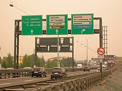 An exit lane sign on an Italian autostrade: destination=Mestre Via Castellana;ospedale;Castelfranco V destination:colour=white;white;blue[3] destination:symbol=centre;hospital;