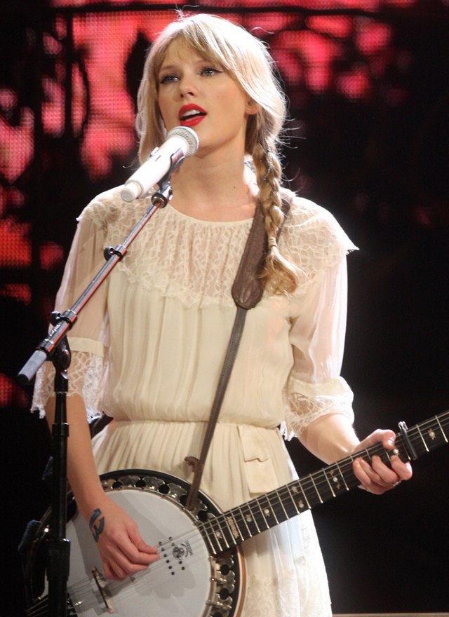 Taylor Swift singing into a mic while playing a banjo