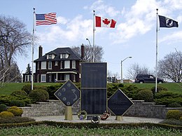 Large brown house behind Canadian and American flags