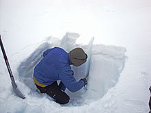 Na fotografii je osoba, která stojí ve vykopané jámě ve sněhu a v hladkém boku dané jámy odřezává z boku sloupec sněhu o rozměrech 30x30 cm