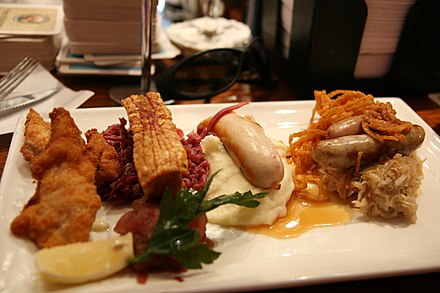 Hearty Bavaria food on a fancy plate.  Left to right: Schnitzel, pork belly (Schweinebauch) with red cabbage (Rotkohl), Weißwurst with mashed potatoes (Kartoffelpüree), Bratwurst on sauerkraut