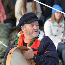 In het kanaal van Sables-d'Olonne, buste, baard, met een zeemanspet op, slaat hij een bodhrán, een Ierse lijsttrommel.