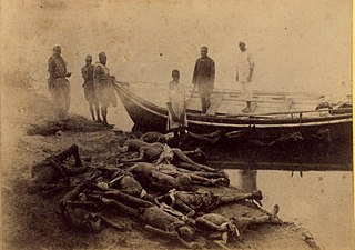 Photographie présentant une dizaine de corps amoncelés sur la berge d'un cours d'eau, six spectateurs se tiennent à l'arrière-plan autour d'une large barque.