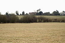 The source of Monks Brook is located under the hedgerow in the foreground of this photograph Monks Brook Source.jpg