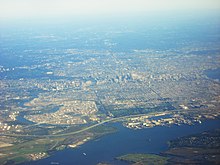 Photographie aérienne de Philadelphie. Au premier plan (sud) : la confluence entre la Schuylkill et le Delaware, la zone industrialo-portuaire ; au second plan, on distingue le plan en damier, le centre des affaires avec ses gratte-ciels ; à gauche : le quartier des universités et le Fairmount Park.