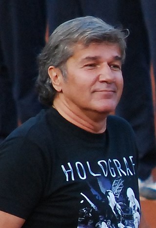 A man wearing a black shirt waliking on a tennis court, with fellow people behind him.