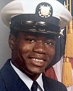 Foto de retrato de Walter Scott en uniforme de la Guardia Costera de los Estados Unidos con una bandera estadounidense parcialmente visible en el fondo.