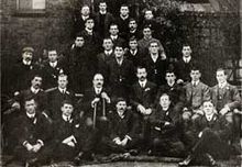 Photographie d'un groupe d'hommes en costume noir disposés sur cinq rangés