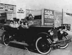 People in a 1917 Jordon Touring car S.Q.R. Store and sign visible, c.1924