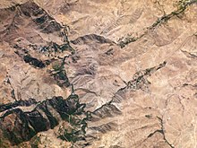 Vista aérea, formaciones ribereñas en los fondos de los valles con unos pocos campos y grupos de viviendas, en un paisaje generalmente árido.