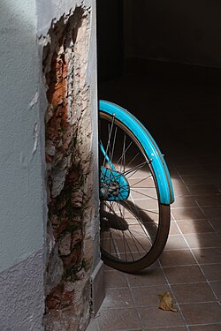 Rear wheel of a blue bike behind wall, Cremona, Italy