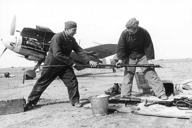 Marseille's service men, Hoffmann (left) and Berger, cleaning the bore of one of the cannons of a Bf 109. "Yellow 14" W.Nr. 8673 can be seen in the ba