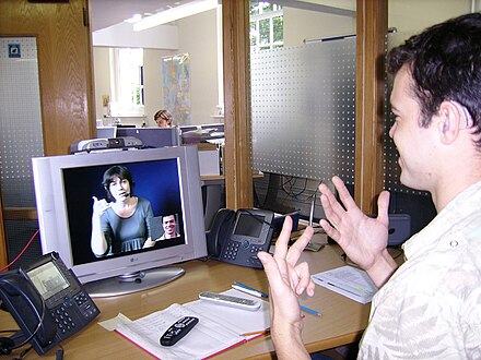 A deaf or hard-of-hearing person at his workplace using a VRS to communicate with a hearing person in London.