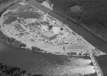 Photo aérienne en noir et blanc, les deux bâtiments cylindriques des réacteurs sont au centre de la photo.