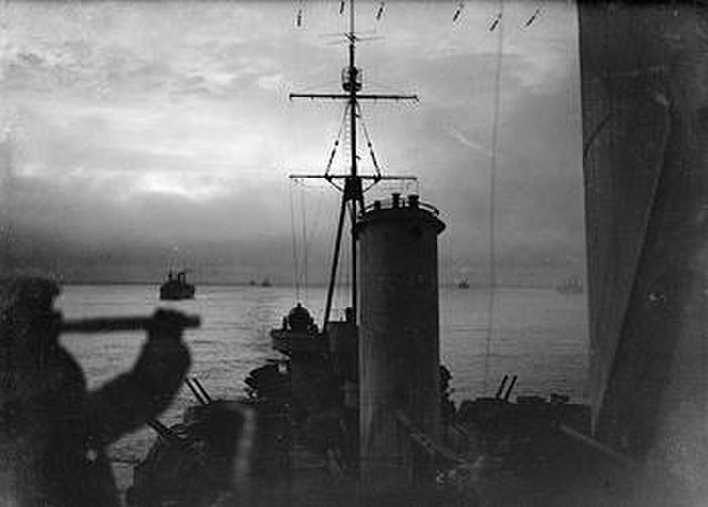 View from the cruiser HMS Sheffield as she sails on convoy duty through the waters of the Arctic Ocean. In the background are merchant ships of the co