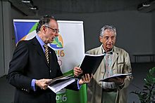 Un hombre de traje entrega libros a otro hombre con un atuendo menos formal.