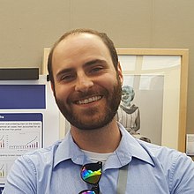 A photo of Claytonllibrar, from roughly the shoulders up. He is a white man with close-cropped brown hair and a short beard, and is wearing a blue collared shirt.