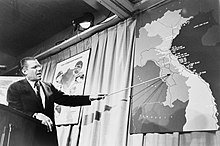Robert McNamara points at a Vietnam map using a pointing stick. Robert McNamera pointing to a map of Vietnam at a press conference, 1965.JPG