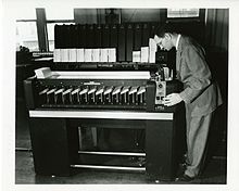 An IBM card sorter performing a radix sort on a large set of punched cards. Cards are fed into a hopper below the operator's chin and are sorted into one of the machine's 13 output baskets, based on the data punched into one column on the cards. The crank near the input hopper is used to move the read head to the next column as the sort progresses. The rack in back holds cards from the previous sorting pass. SEACComputer 038.jpg